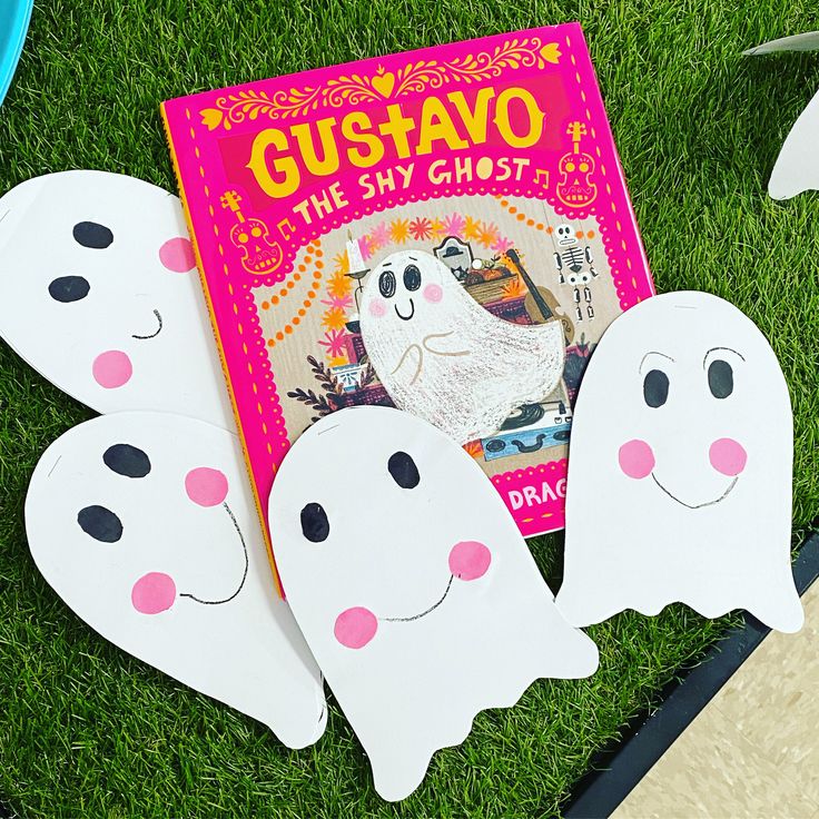 some paper ghost cutouts are laying on the grass next to a children's book