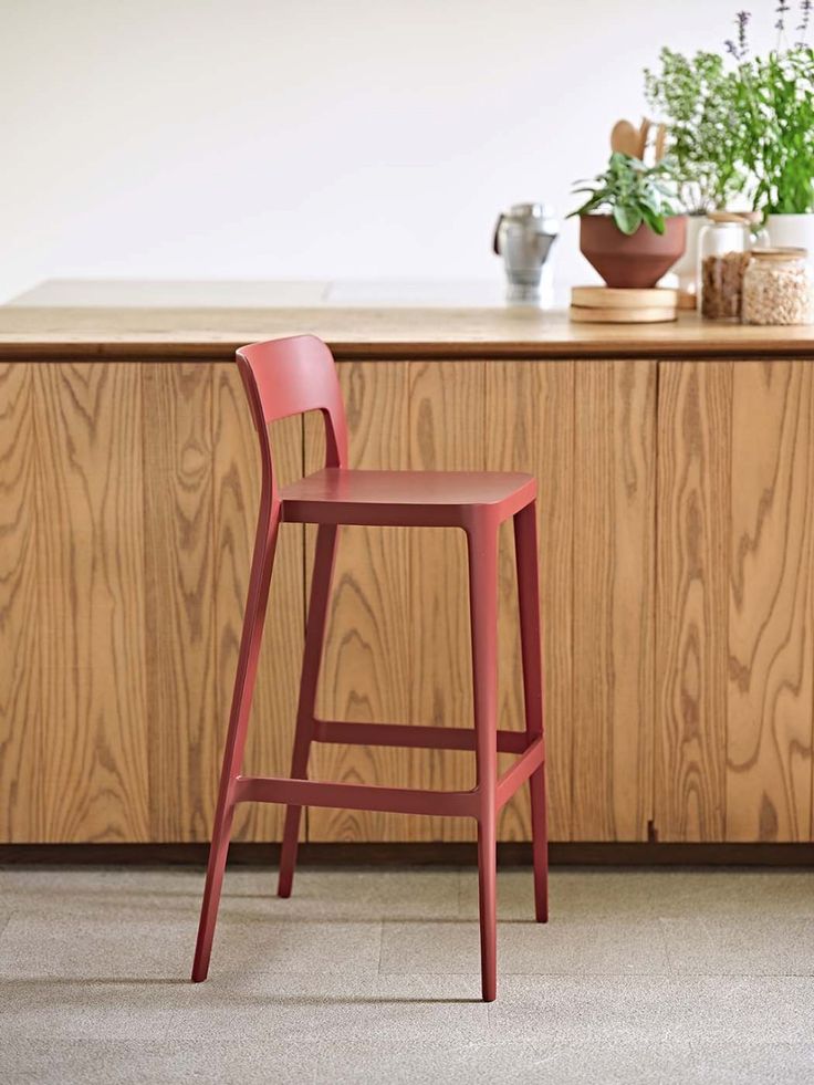 a red stool sitting in front of a counter top next to a potted plant