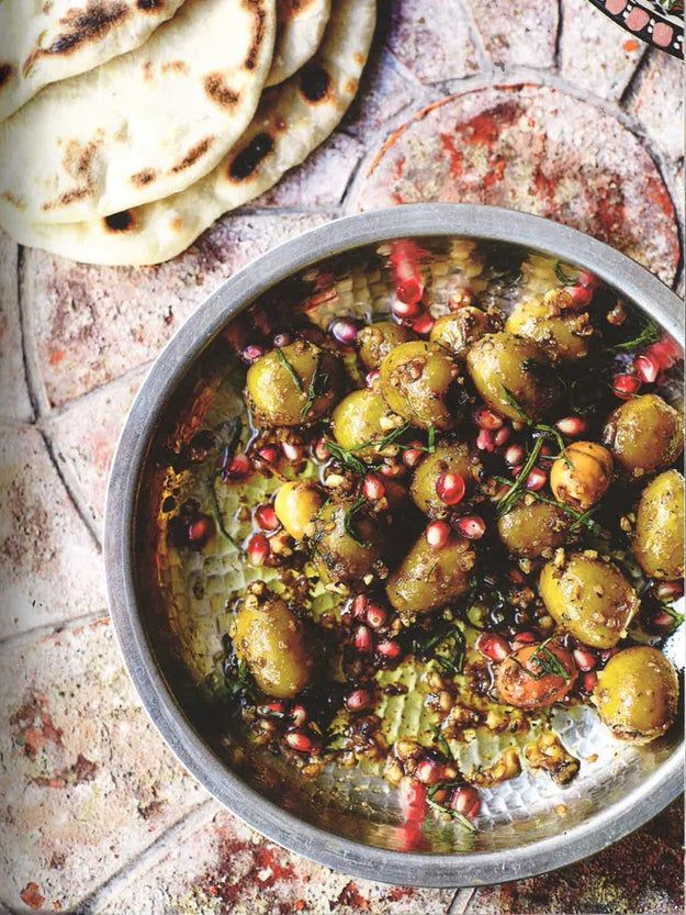 a metal bowl filled with food next to pita bread on top of a table