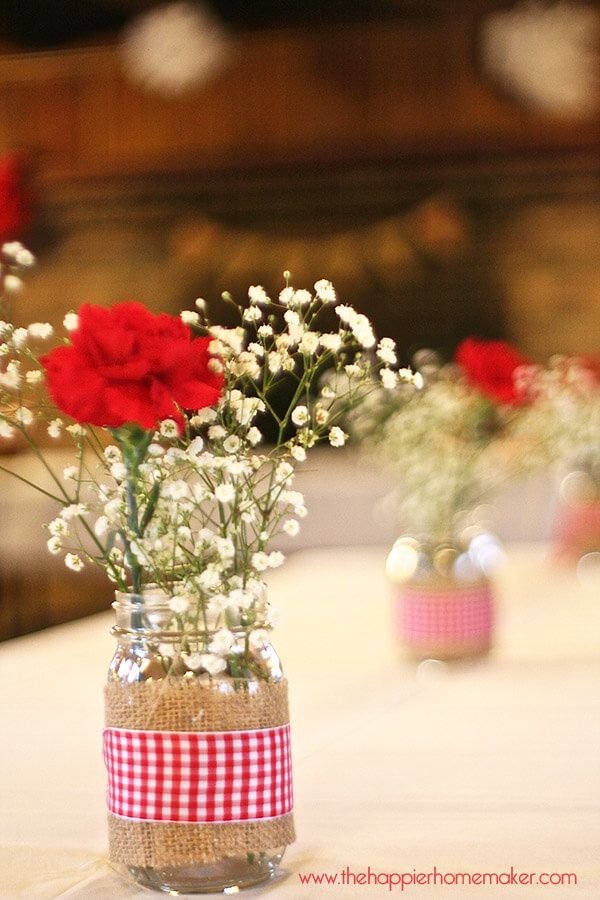 red and white flowers are in a mason jar on a table with other vases