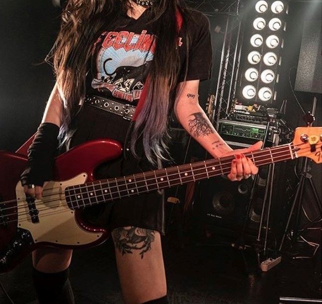 a woman with long hair and piercings holding a bass in front of a stage