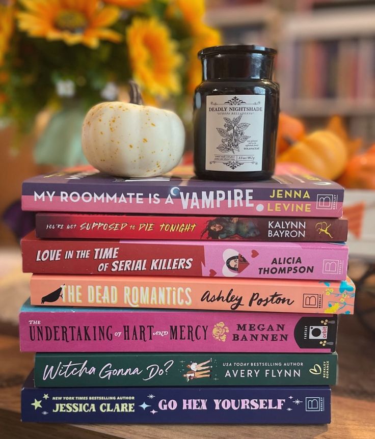 a stack of books sitting on top of a wooden table next to a jar of candle