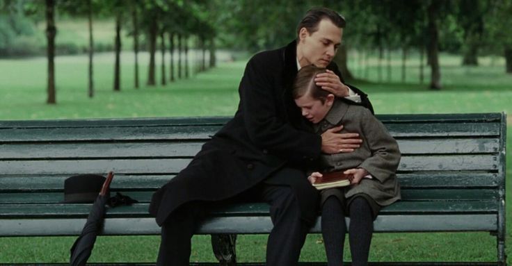 two people sitting on a park bench with one person hugging the other's head