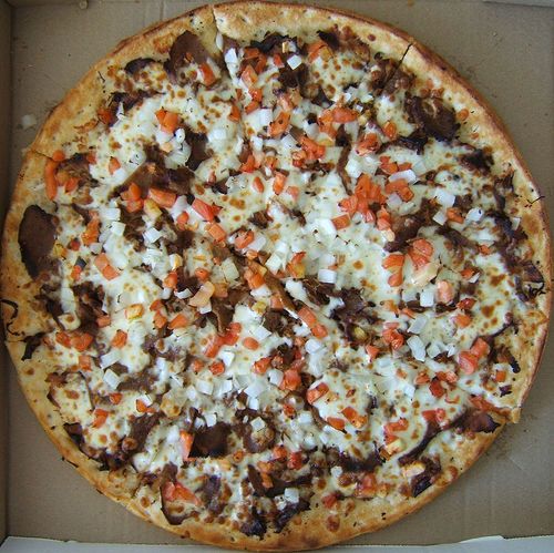 a pizza with carrots, onions and other toppings in an open cardboard box