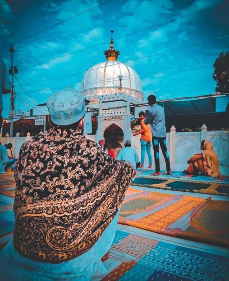 people are sitting on the ground in front of a white building with a dome and blue sky