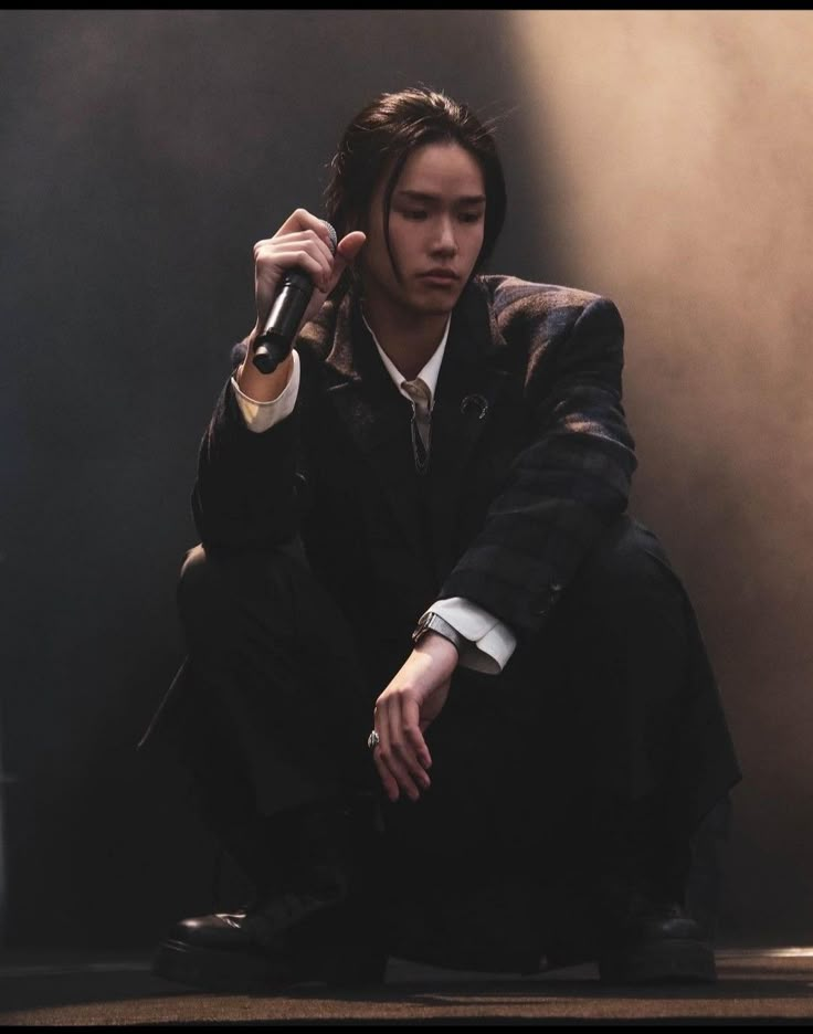 a young man sitting on the ground with a microphone in his hand and wearing a suit