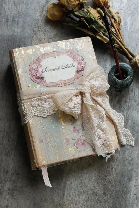 an old book with lace and flowers on it sitting next to a flower pot filled with dried flowers