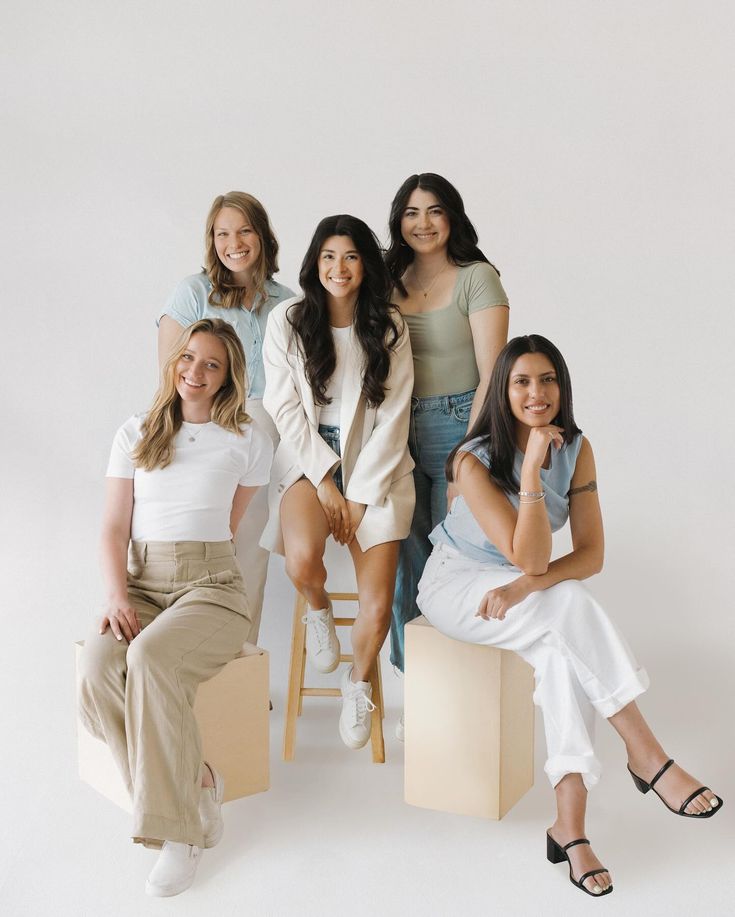 a group of women sitting next to each other in front of a white wall and posing for the camera