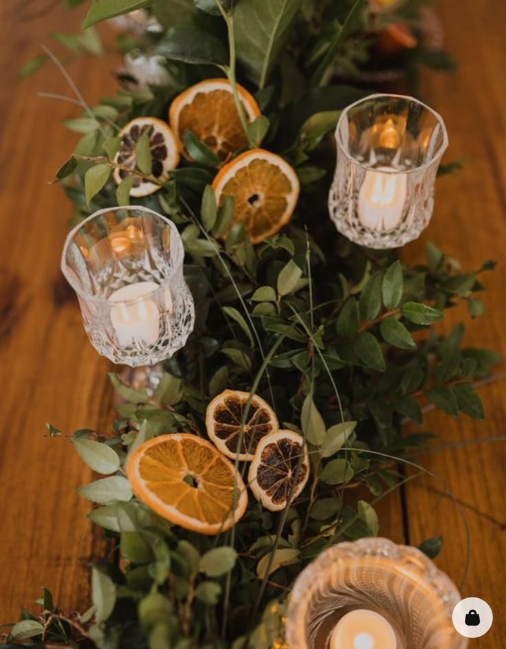 an arrangement of oranges and candles on a table with greenery, leaves and flowers