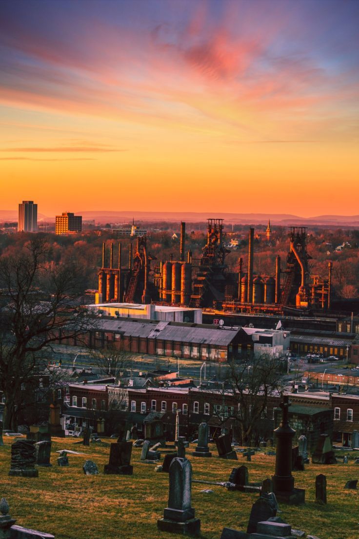 a cemetery with many headstones in the foreground and buildings in the background at sunset