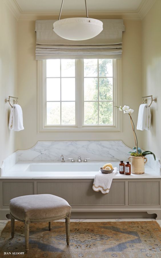 the bathroom is decorated in white and has a large bathtub with two windows above it