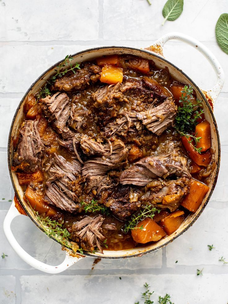 a pot filled with meat and vegetables on top of a white tile floor next to green leaves