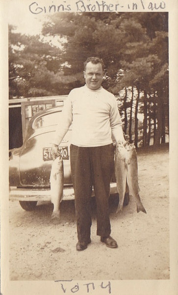 an old black and white photo of a man holding two fish in front of a car