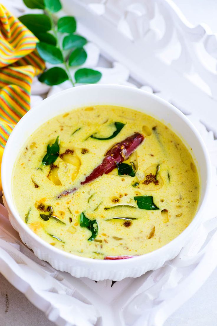 a white bowl filled with yellow soup and garnished with green leaves on top