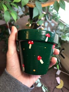 a hand holding a green cup with red mushrooms on it