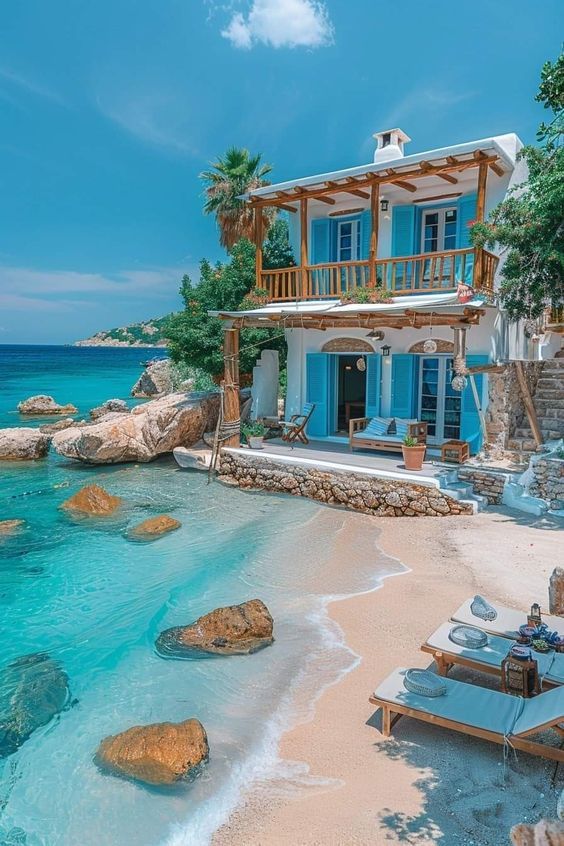 a house sitting on top of a sandy beach next to the ocean with lounge chairs