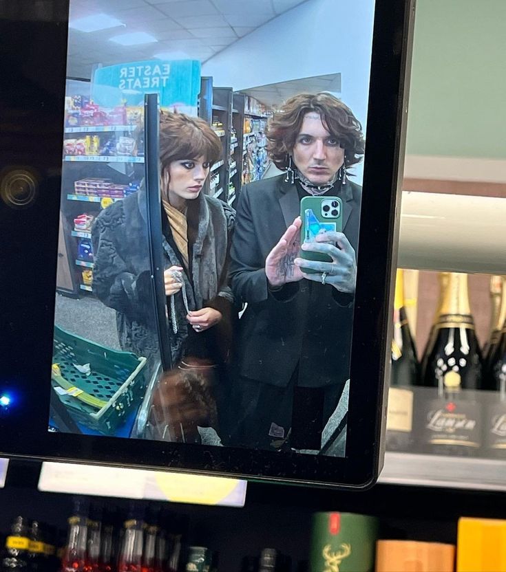 a man and woman taking a selfie in front of a mirror with liquor bottles behind them