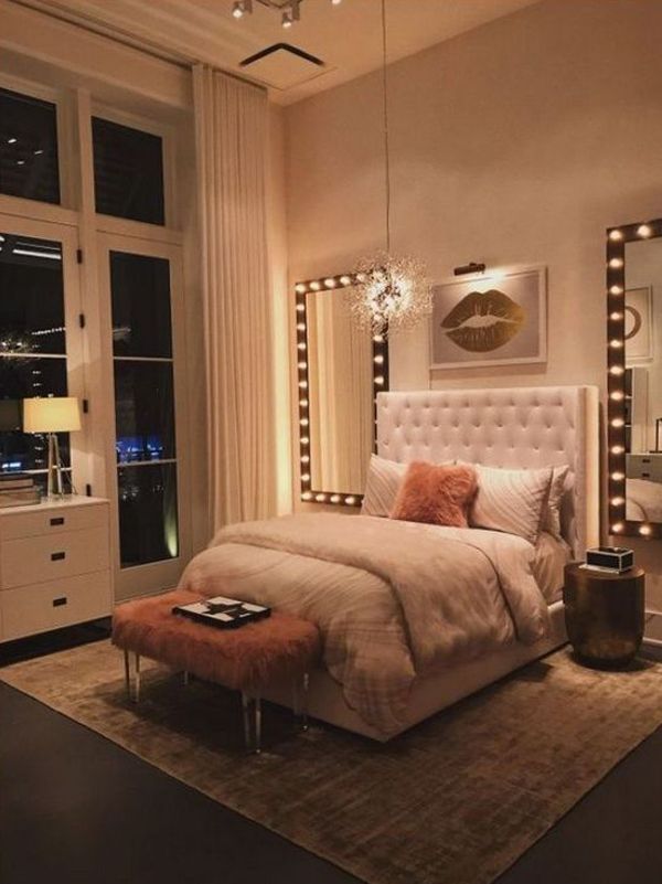 a bedroom with a large bed and lights on the wall above it, along with an ottoman