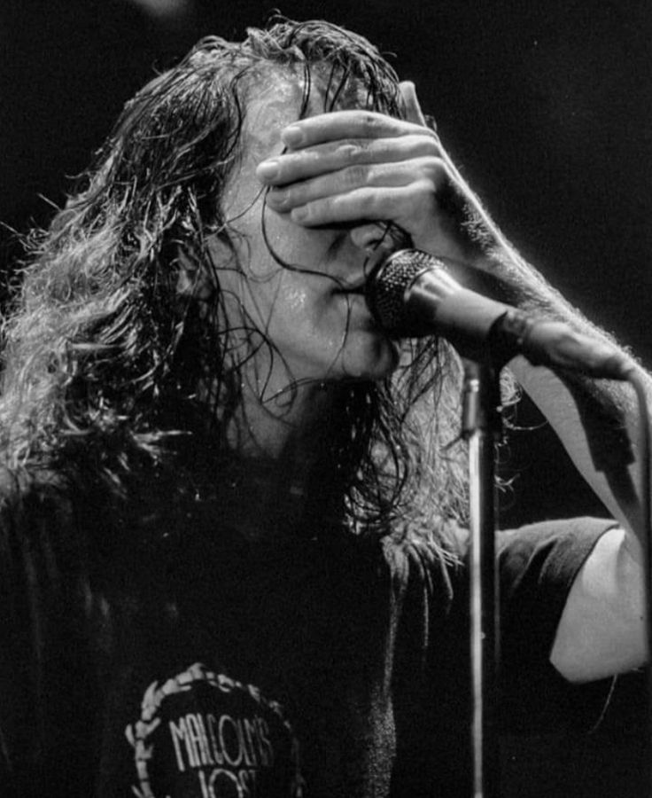 a man with long hair holding his head to his face while standing in front of a microphone