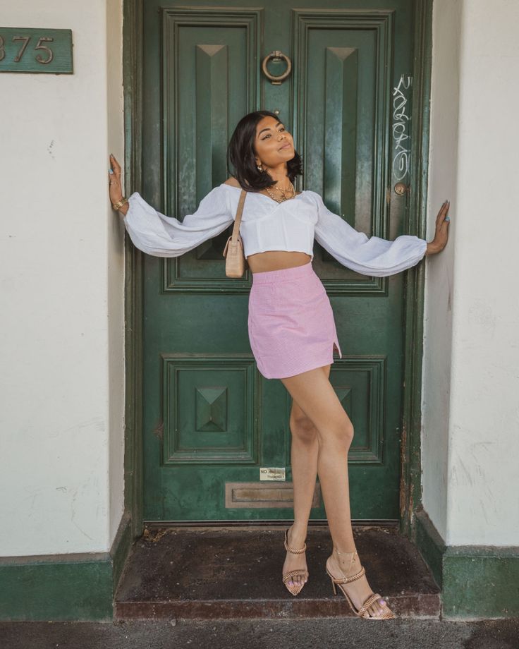 a woman standing in front of a green door with her arms outstretched and legs crossed