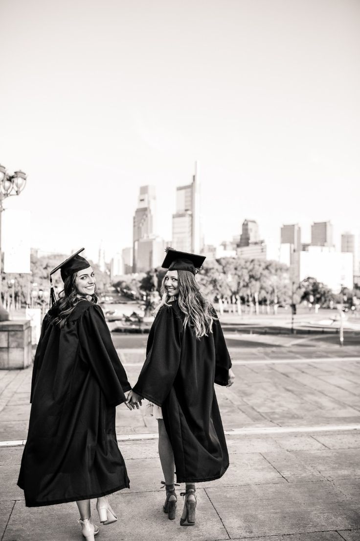 two women in graduation gowns holding hands and walking down the street with their caps and gowns on