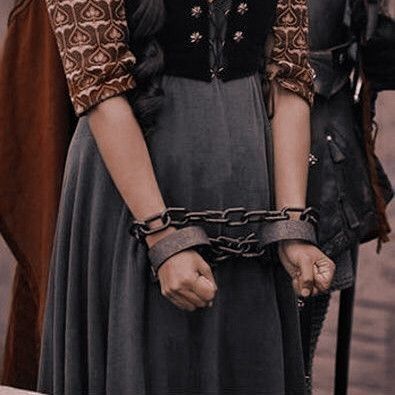 a woman in a long dress with a chain around her neck and hands on her hips