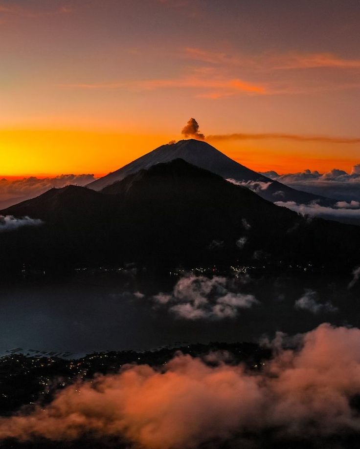 the sun is setting over a mountain with clouds below it and in the foreground