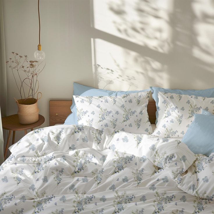 an unmade bed with blue and white flowers on the comforter, next to a window