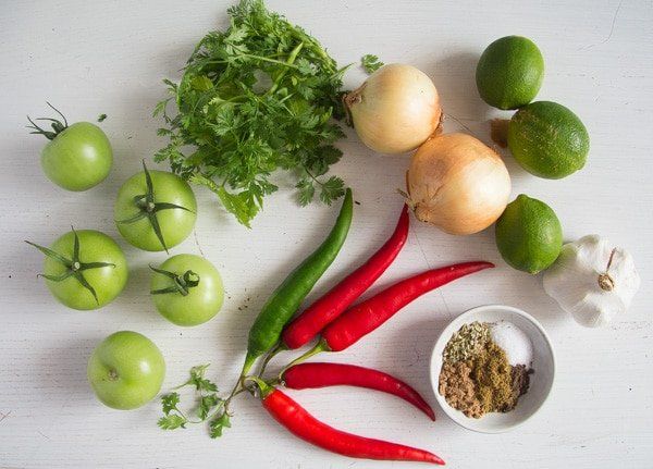 various vegetables are arranged on a white surface, including tomatoes, peppers, and limes