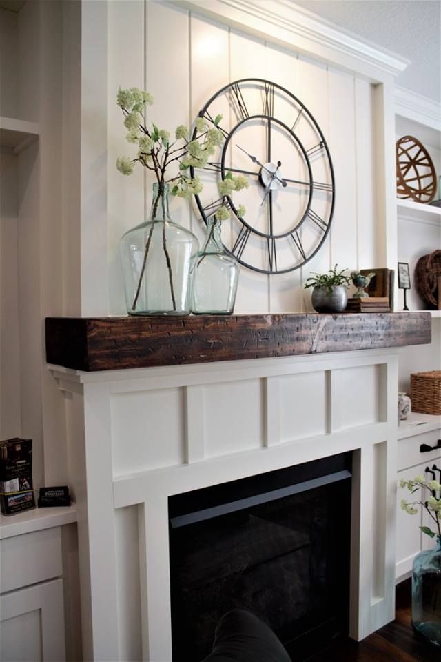 a clock mounted to the wall above a fireplace with vases and flowers on it