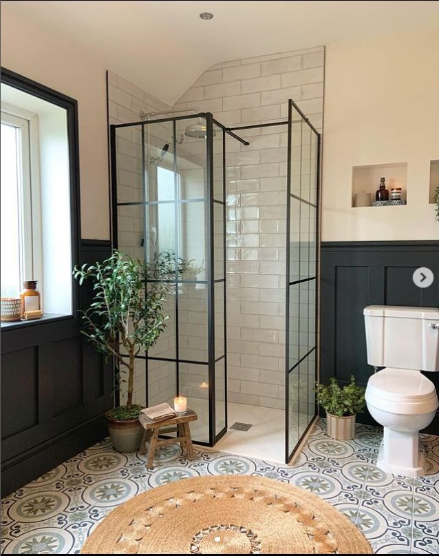 a white toilet sitting next to a shower in a bathroom under a window with a potted plant on top of it