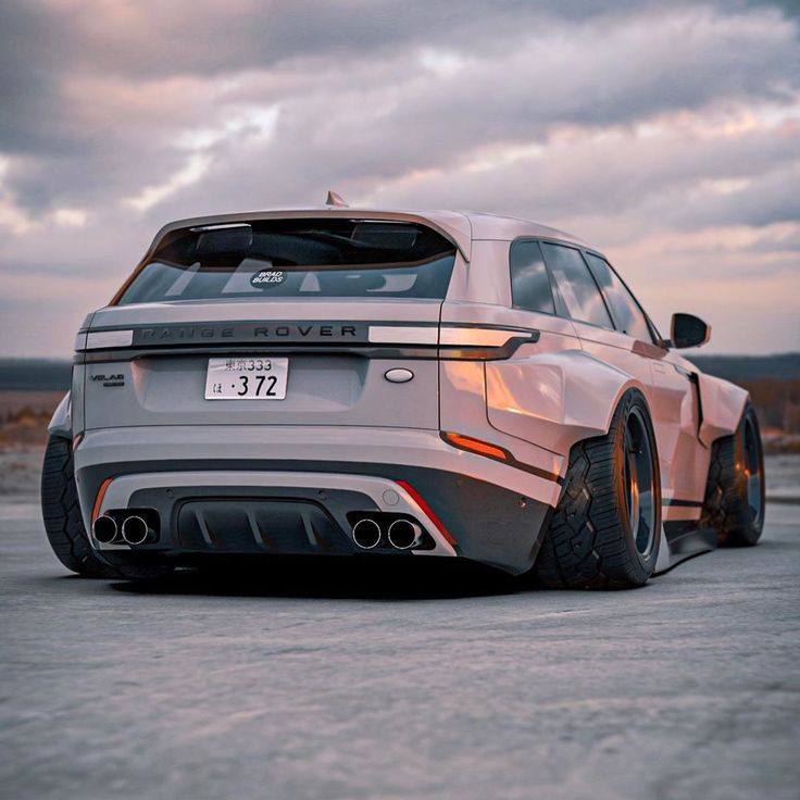 the rear end of a white car parked on top of a parking lot at sunset