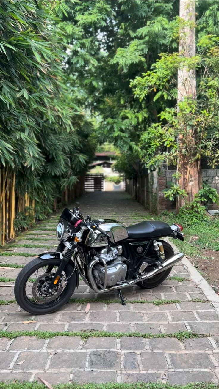 a black motorcycle parked on top of a brick walkway next to trees and bushes in the background