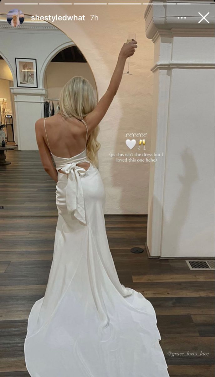 the back of a woman in a white dress with her hand up to the ceiling