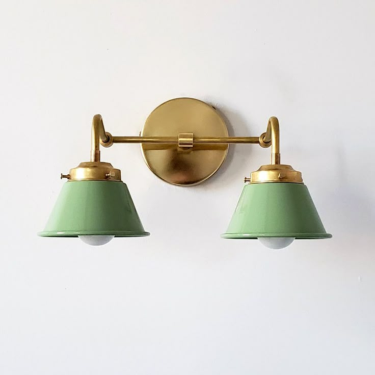 two green lamps are on the wall in front of a white wall and light fixture