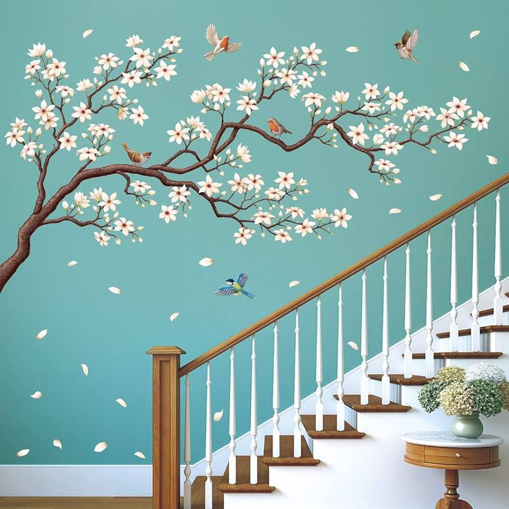 a tree with white flowers and birds on it next to a stair case in front of a blue wall