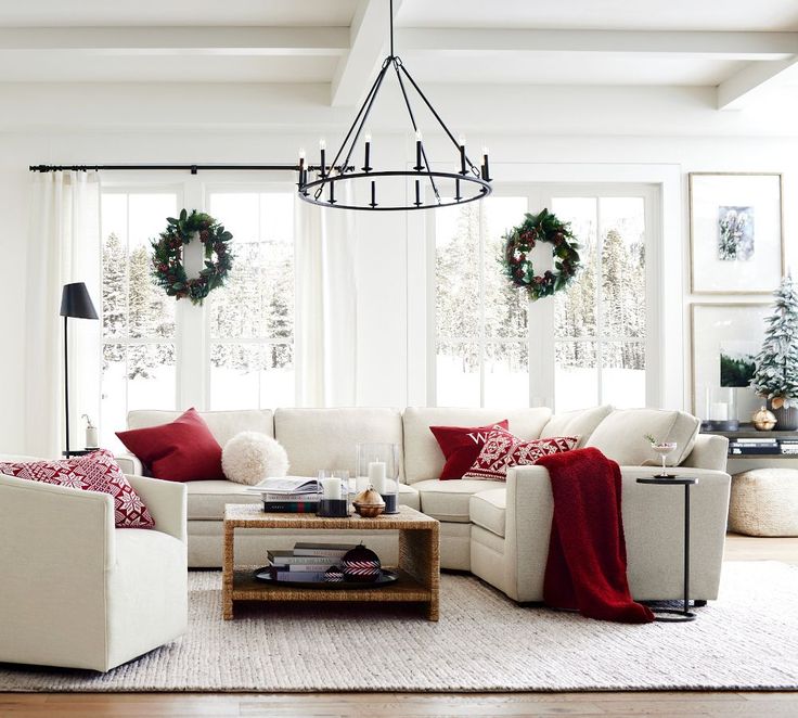 a living room filled with white furniture and christmas wreaths on the windows sill