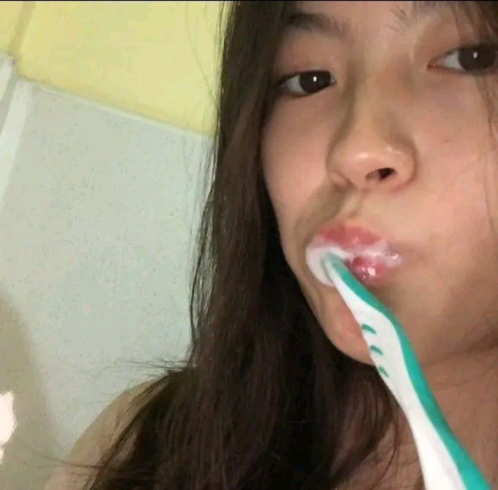 a girl brushing her teeth with a green and white toothbrush