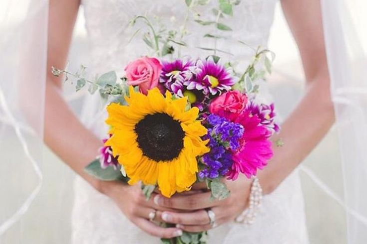 a bride holding a bouquet of sunflowers and other flowers on her wedding day