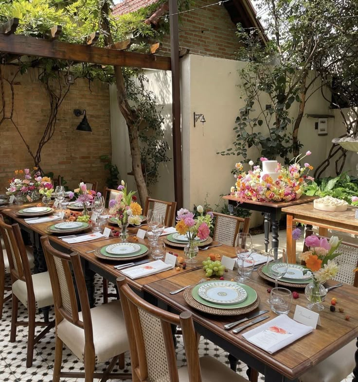 an outdoor dining table set with place settings and flowers in vases on the tables