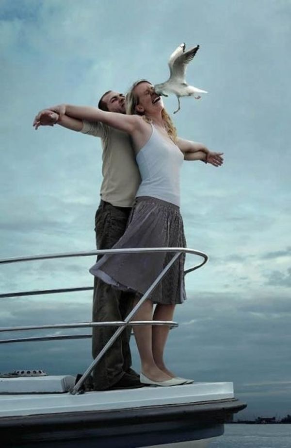 a man and woman standing on the deck of a boat with seagulls flying overhead