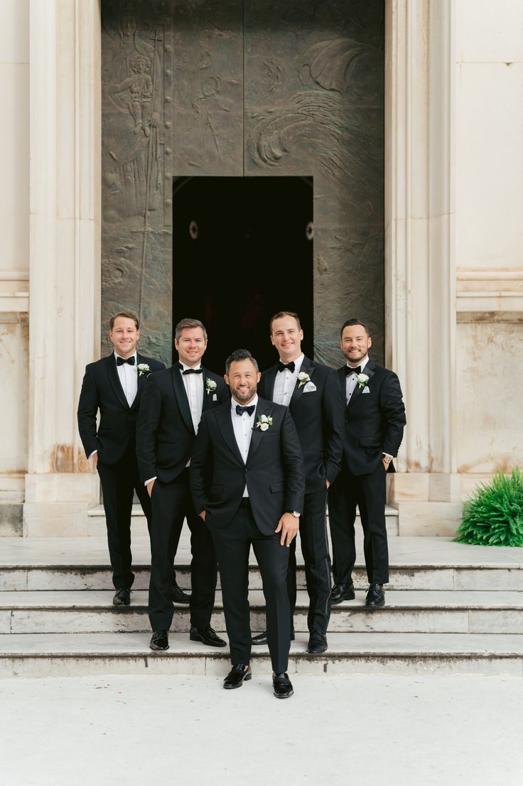 a group of men standing next to each other in front of a door wearing tuxedos