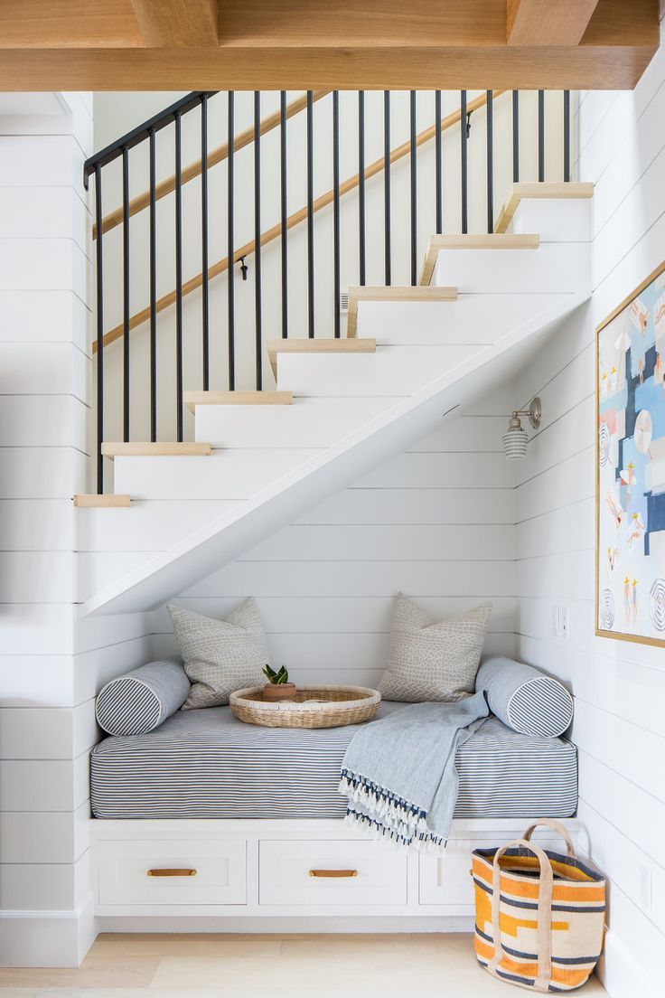 there is a small bed under the stairs in this room with white walls and wood flooring