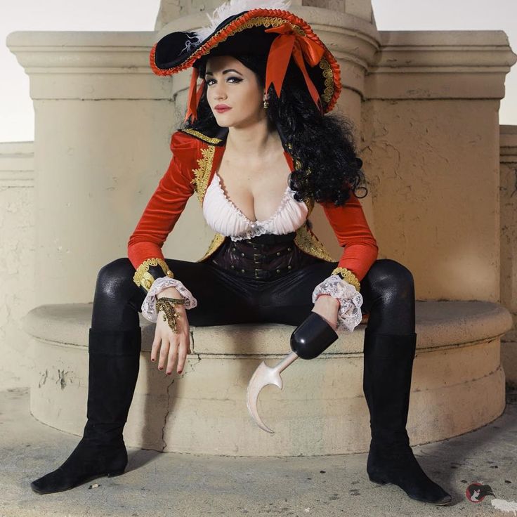 a woman in a pirate costume sitting on a stone pillar with her legs crossed and wearing black boots