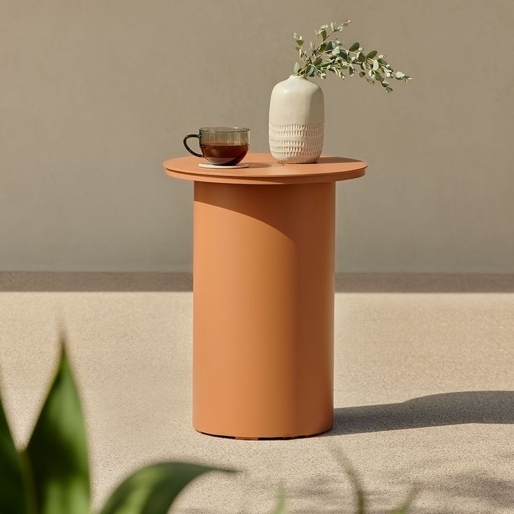 a small table with a vase and cup on it next to a potted plant