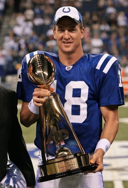 a football player holding up a trophy on top of a field with another person standing next to him