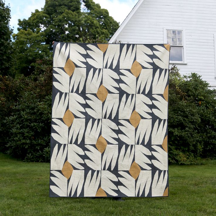 a black and white quilt sitting on top of a green grass covered field next to a house