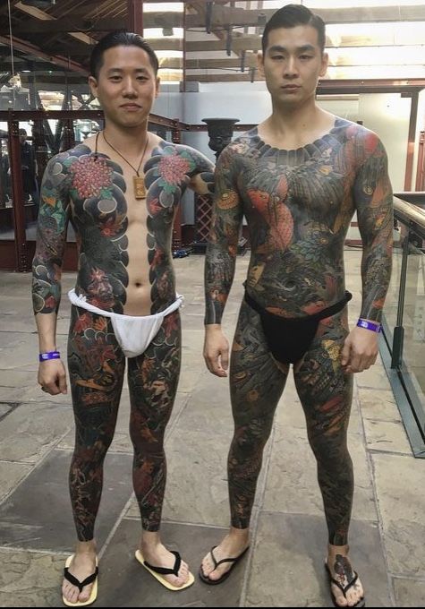 two men standing next to each other with tattoos on their arms and bodysuits