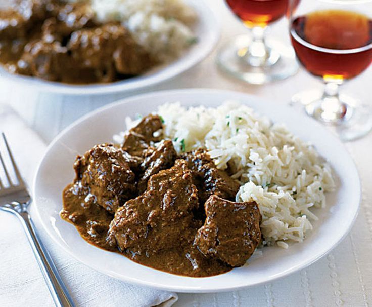 two plates with meat and rice next to wine glasses