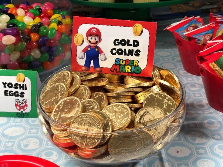 a bowl filled with gold coins on top of a table next to red plates and candy